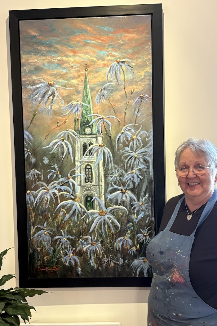 Diane pose à droite d’une toile, sur laquelle on voit l’aster à feuilles de linaire devant la cathédrale de Trois-Rivières