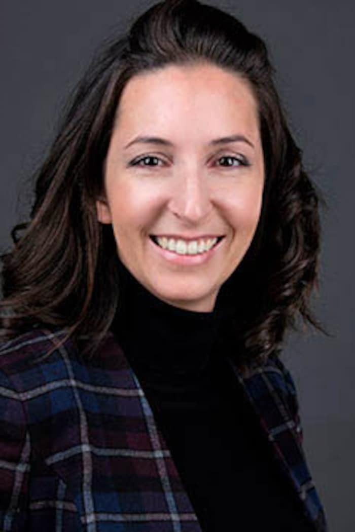 Portrait d'une femme, souriante, aux cheveux bruns et portant un veston. 