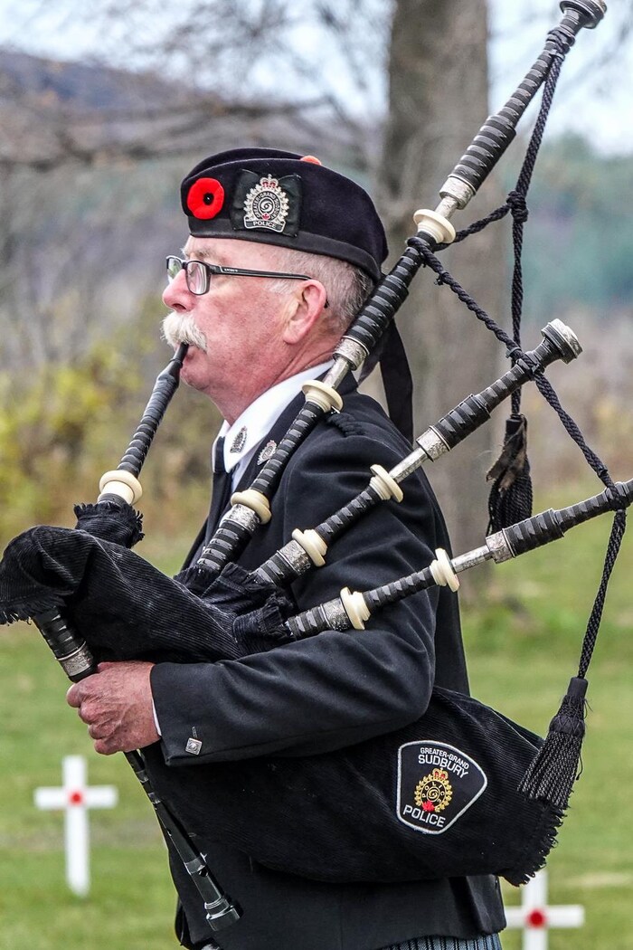 Un musicien souffle dans sa cornemuse devant un ancien combattant qui porte le drapeau du Canada.