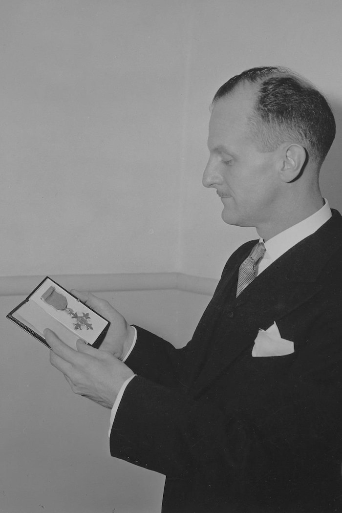 Marcel Ouimet pose en regardant son insigne de l'Ordre de l'Empire britannique placé dans un coffret.