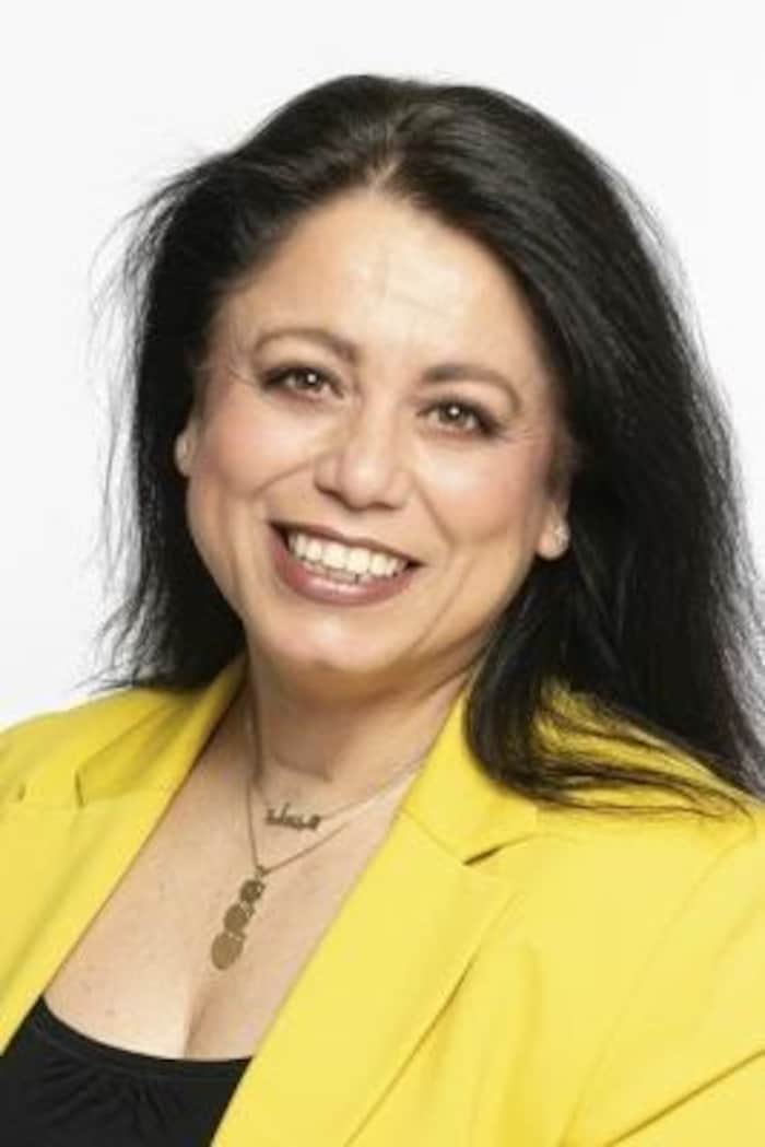 Une femme souriante prend la pose. Elle porte un veston jaune et un chandail noir. 