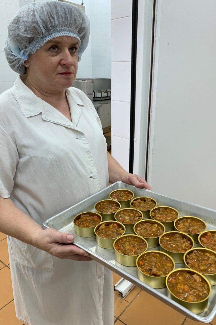 On voit une employée du laboratoire russe qui transporte sur un plateau de la nourriture en conserve destinée aux cosmonautes.