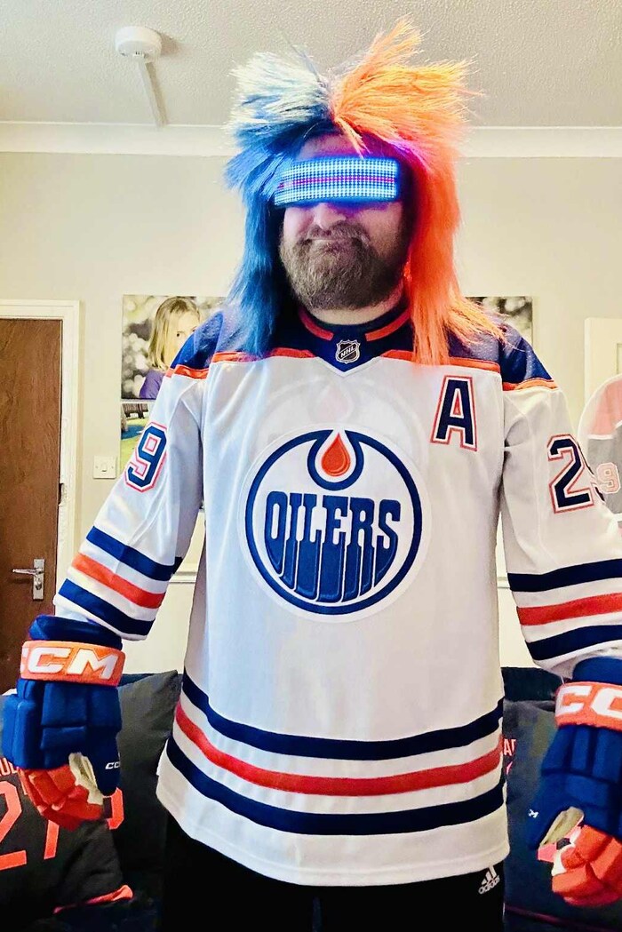 Un homme avec une perruque et un maillot des Oilers d'Edmonton dans son salon.