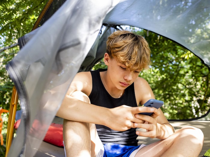 Un adolescent regarde son téléphone sous une tente.