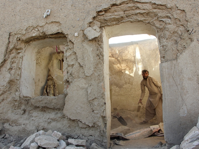Un homme, debout dans sa maison détruite par une frappe, tient un morceau de béton dans sa main .