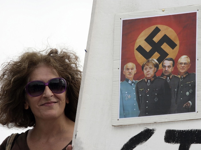 Une manifestante tient une pancarte sur laquelle on voit un montage d'Angela Merkel et d'autres dirigeants en uniforme SS sur fond de drapeau nazi.