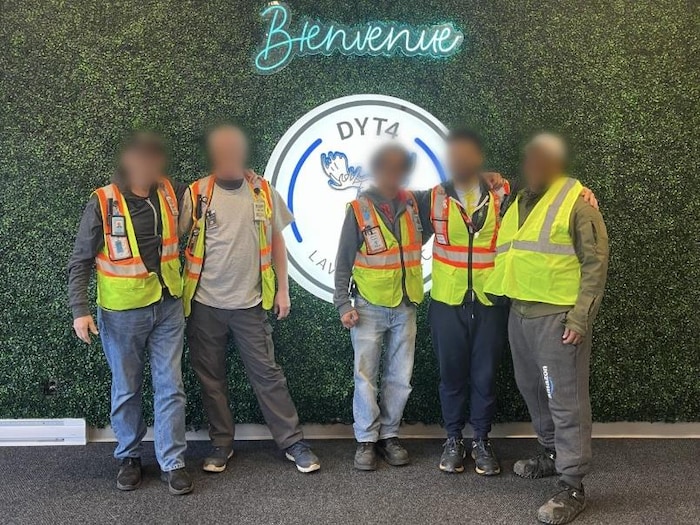 Cinq travailleurs posent devant une affiche qui porte le mot bienvenue.