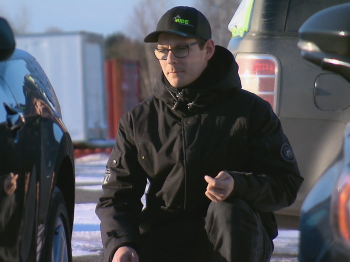 Un homme portant un manteau d'hiver est agenouillé près d'un véhicule et l'observe. 