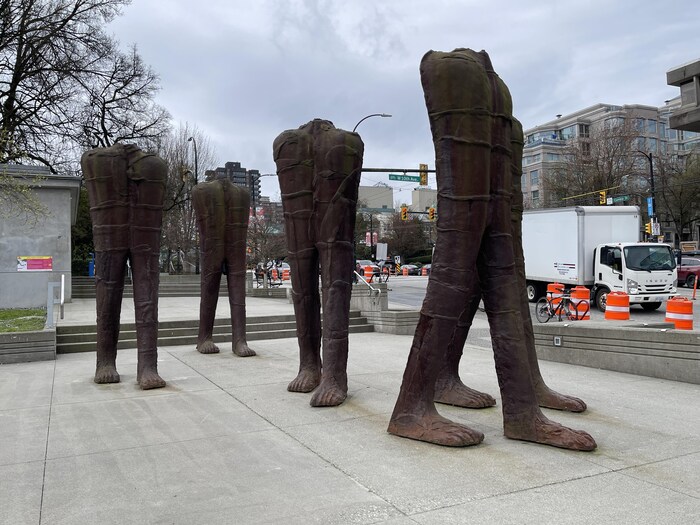 Des sculptures représentant de longues jambes sont installées près d'une rue passante.