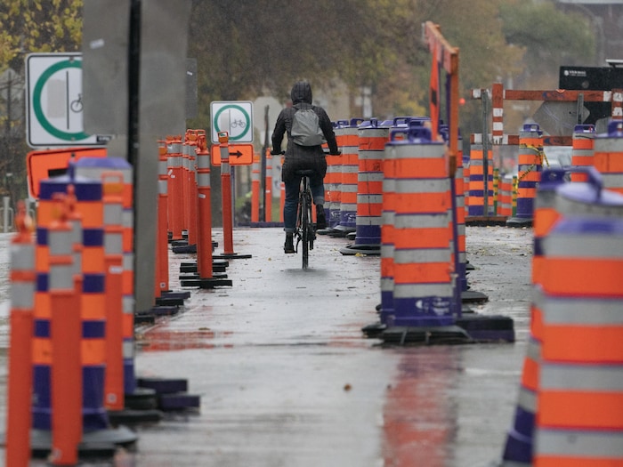Un cycliste circule sur une rue où il y a des travaux et de nombreux cônes orange.