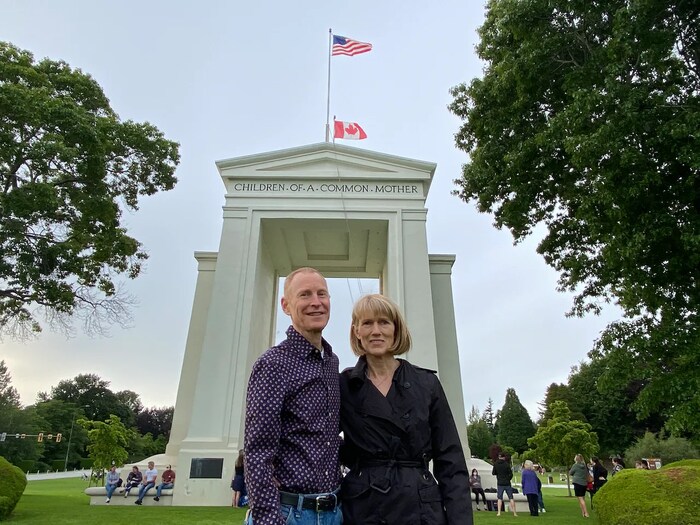Nakatayo sina Birgit Heinbach at Ian Geddes sa harap ng US-Canada border.