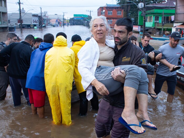 Une femme est portée par un membre d'une équipe de secours au milieu d'une rue inondée.