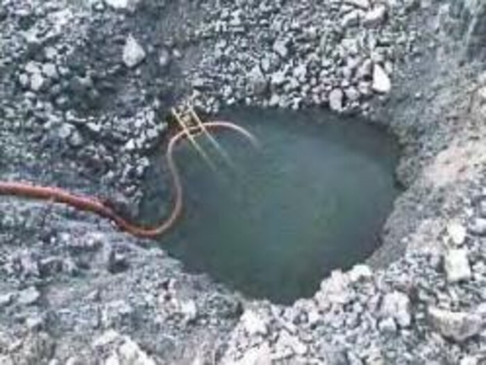 Un trou rempli d'eau avec une échelle et un boyau d'arrosage dans une aire d'extraction de la carrière Sintra.