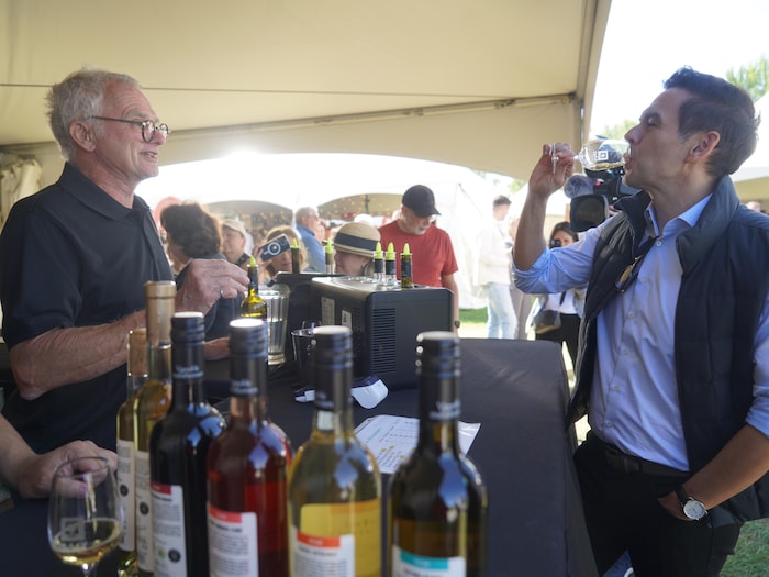 Charles Milliard boit du vin en discutant avec un homme sous un chapiteau.
