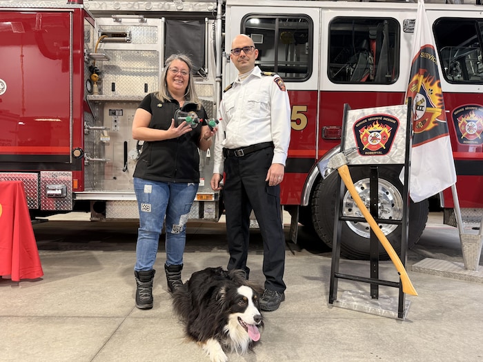 Une femme, un pompier et un chien sont devant un camion de pompiers.