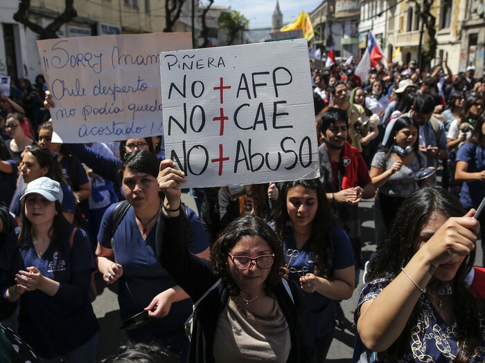Une femme, devant une foule, tient une pancarte qui dit «Fin aux abus».