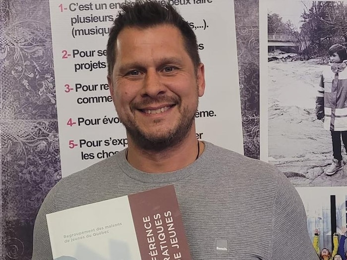 Le directeur de la Maison des jeunes le Trèflerie, Christian Caissy, tient un livret dans ses bras et est souriant.