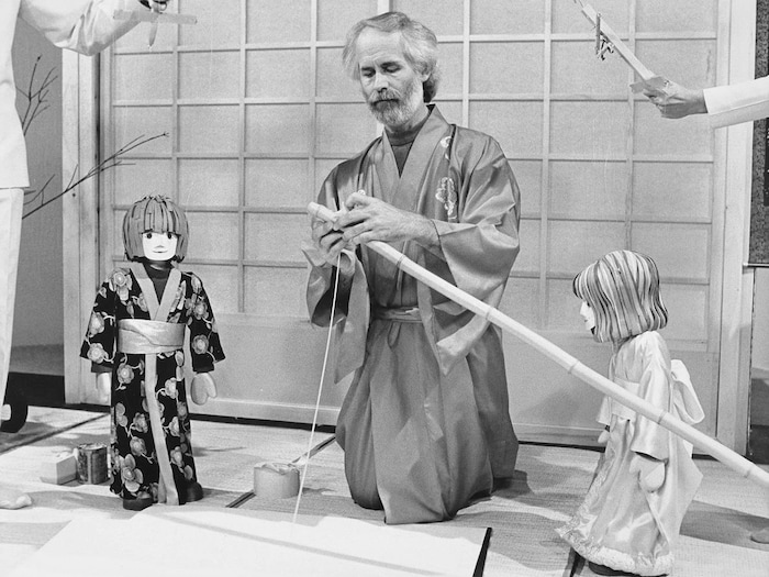 L'animateur Claude Lafortune en kimono tout comme les deux marionnettes qui l'accompagnent dans un décor japonais.