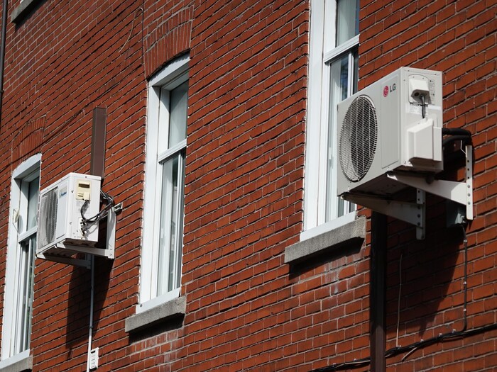 Deux climatiseurs accrochés sur un immeuble en brique.