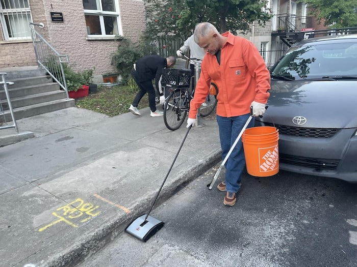 Un homme tenant un bac en plastique passe le balai dans la rue.