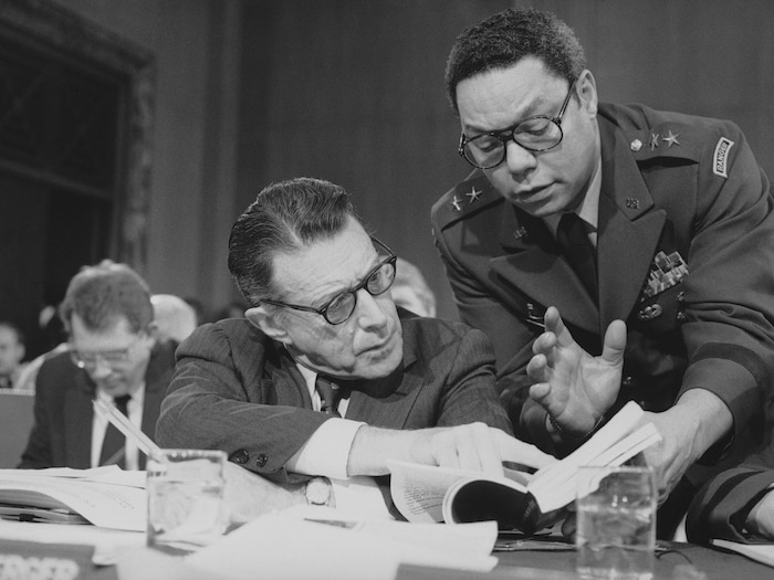 Les deux hommes consultent des documents et discutent ensemble.