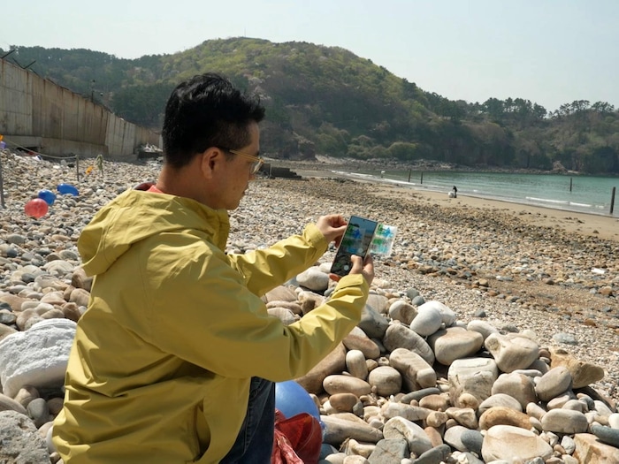 Sitting on the beach, Kang Dong-Wan sweeps a QR code using his phone. understand life north korea thanks