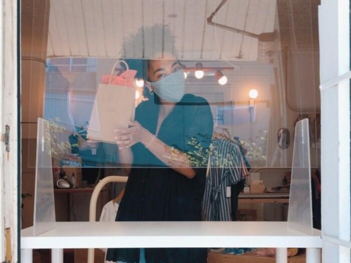Une employée de la boutique Station Service portant un masque est photographiée derrière une paroi de plexiglas.