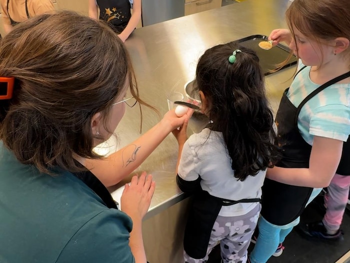 Une petite fille casse la coquille d'un oeuf avec un couteau à beurre.