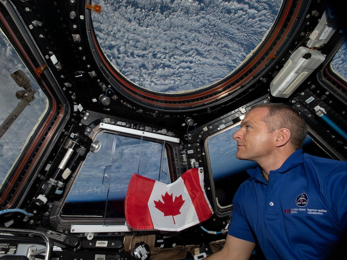 Il regarde la Terre par une fenêtre de la Station spatiale internationale.