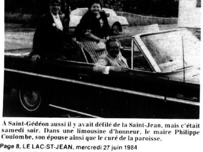 Cette coupure de presse en noir et blanc de 1984 montre trois personnes souriantes à bord d'une voiture décapotable lors du défilé de la Saint-Jean à Saint-Gédéon. Le texte en dessous identifie le maire Philippe Coulombe, son épouse et le curé.