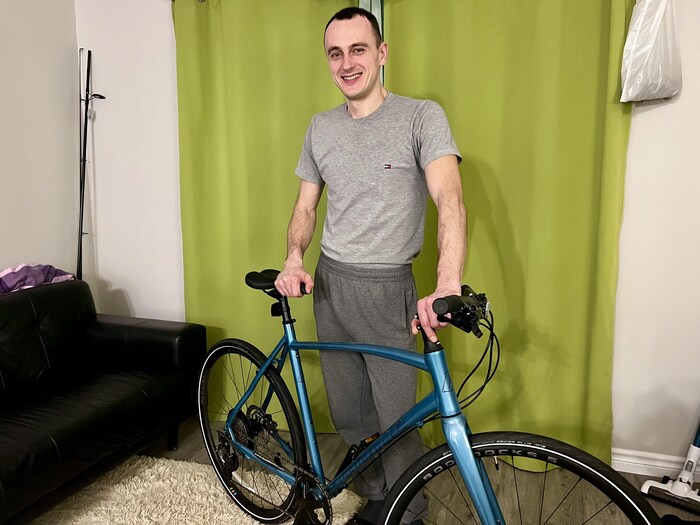 Un homme debout derrière un vélo bleu dans un salon.