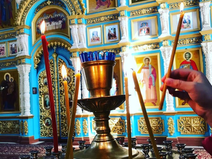 Une main pose une chandelle allumée dans un lieu de culte orthodoxe.
