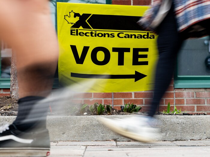 Des personnes marchent devant une affiche d'Élections Canada.