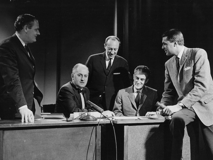 Raymond Lebrun, Paul-Marcel Raymond, Jean-Maurice Bailly, René Lecavalier et Richard Garneau, réunis autour d'un bureau avec micro.