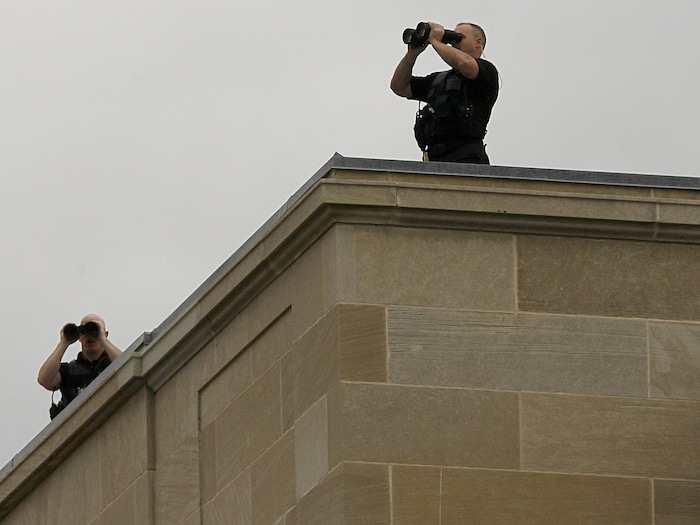 Deux hommes munis de jumelles montent la garde sur un toit.