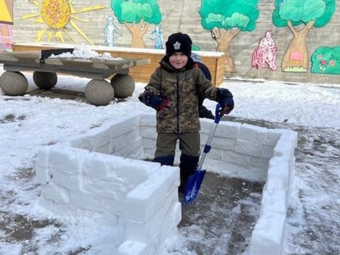Un petit garçon construit un fort avec des blocs de neige dans la cour d'une résidence.