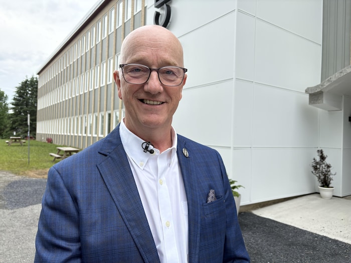 Debout à l'extérieur devant un bâtiment, Gérald Arseneault sourit en regardant vers la caméra.