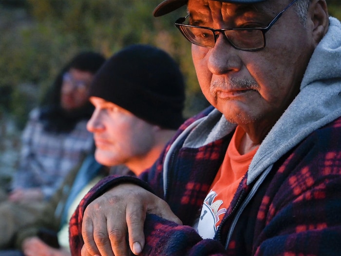 Un gardien innu et un astronaute écoutent des histoires traditionnelles autour d'un feu de camp.