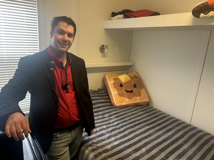 Un homme debout à côté d'un lit.