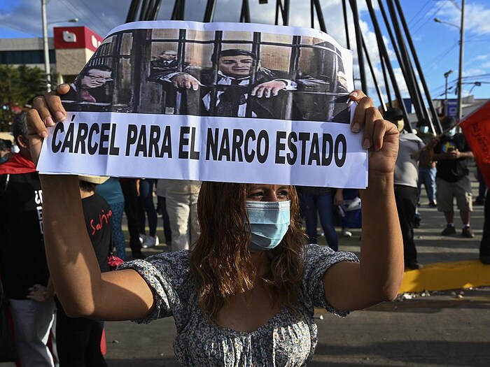 Entourée d'autres manifestants, une femme tient une pancarte qui montre le président du Honduras, Juan Orlando Hernandez, en prison.