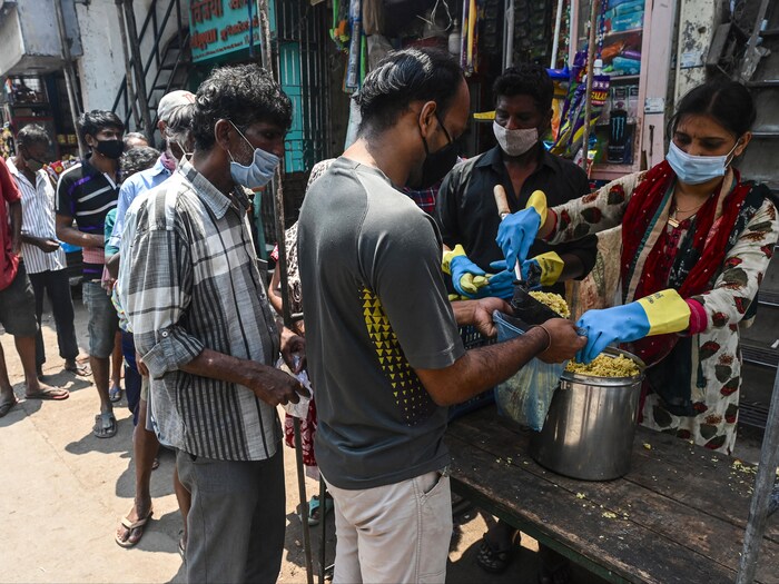 Une file d'hommes se forme devant un kiosque où une femme et un homme servent un plat de riz.