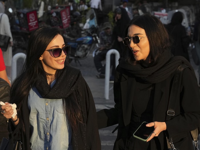 Deux femmes avec de longs cheveux et des lunettes de soleil se promènent dans la rue. 