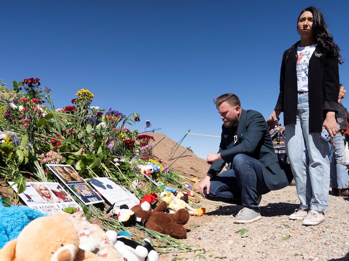 Un homme et une femme, visiblement tristes, regardent les fleurs et les peluches déposées en solidarité avec les victimes de Jeffrey Epstein.