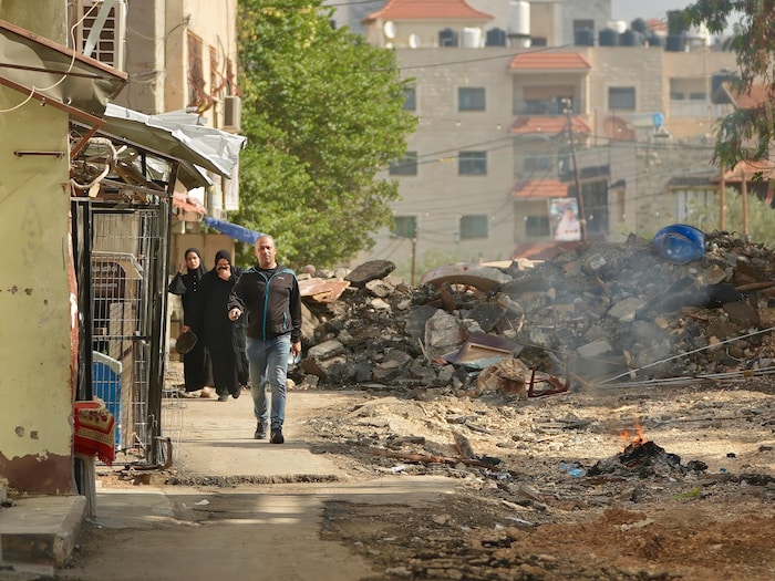 Un homme et deux femmes marchent dans une rue à côté d'un immeuble en ruines. 