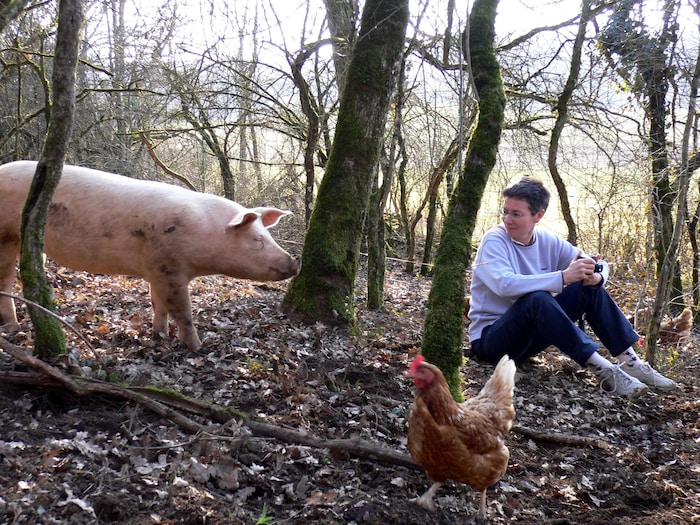 Jocelyne Porcher assise dans le bois à côté d'un cochon et d'une poule.