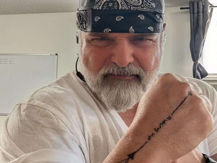 Jonathan Poirier porte une barbe et fixe la caméra en montrant son bras tatoué.
