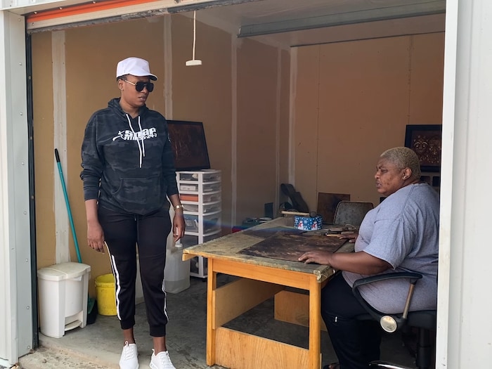 La batteuse de cuivre Joséphine Tambwe Feza Kabibi, assise à une table dans son atelier,discute avec sa fille Nastra Molowayi.