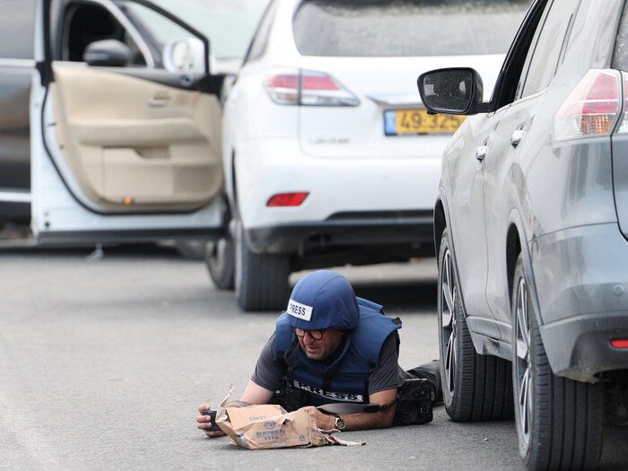 Un homme portant un casque et un gilet pare-balles est allongé face contre terre à côté d’une voiture.