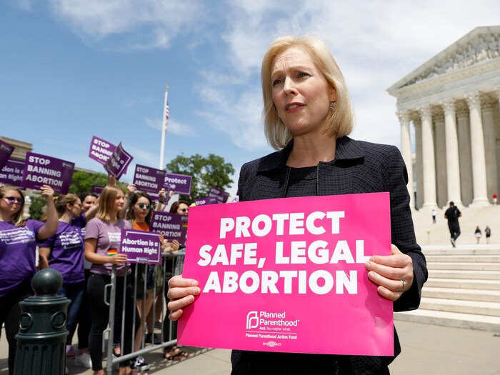 Mme Gillibrand pose devant l'édifice de la Cour suprême, avec une pancarte réclamant de protéger la sécurité et la légalité des avortements.