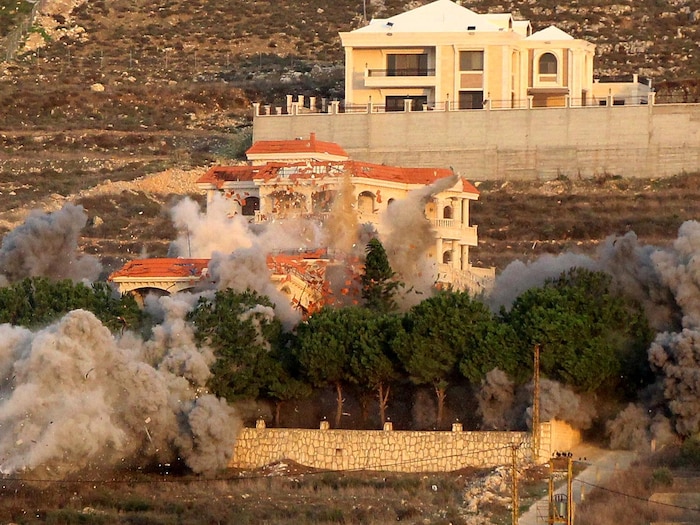 Une épaisse fumée se dégage d'une maison prise pour cible par une frappe et des débris de l'édifice sont projetés sous la force de l'explosion.